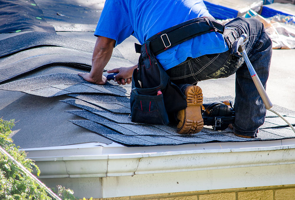 repairing the roof of a home; A worker replaces shingles on the roof of a home