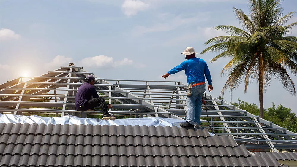 Roof repair, worker with white gloves replacing gray tiles or shingles on house with blue sky as background